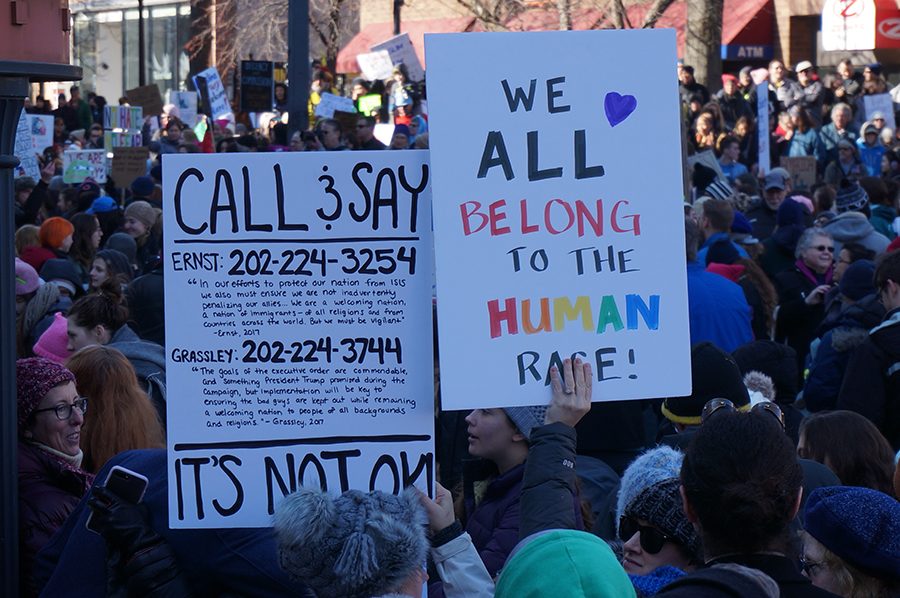 Protesters hold signs displaying messages of unity and action. 