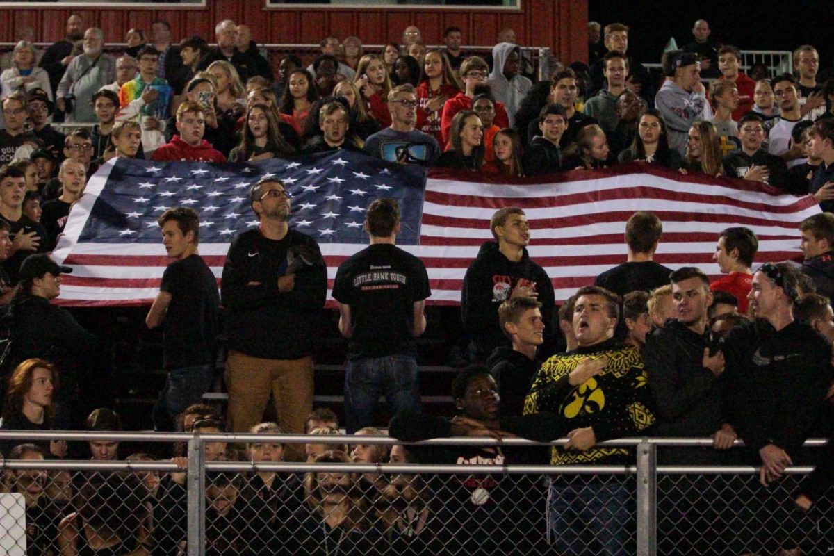 At+the+varsity+football+game+student+protestors+knelt+while+counter-protestors+held+a+flag+behind+them.++Assistant+Principal+Scott+Jespersen+stands+in+between+the+protests.