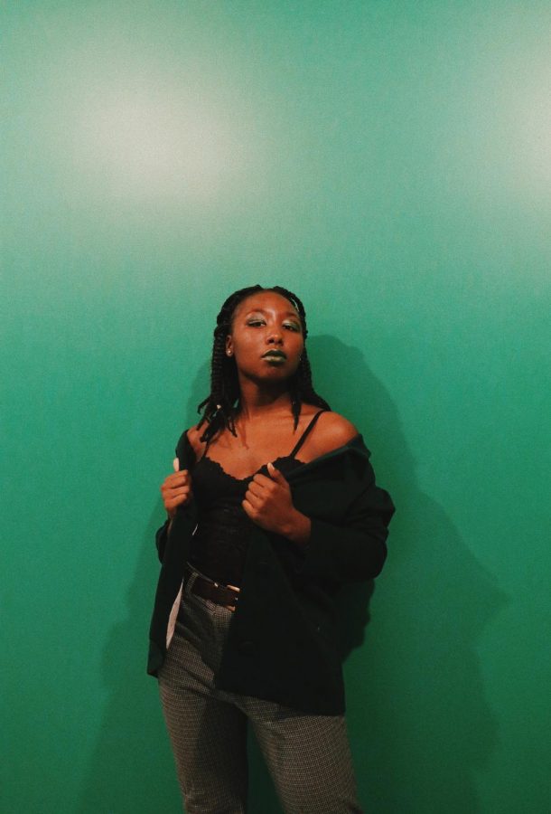 Virginia Muturi 19 poses in front of green wall. 