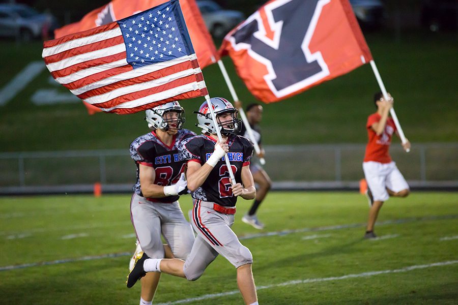 Max DePrenger '19 runs with the American Flag while the rest of the varsity team follows behind him onto the field.
