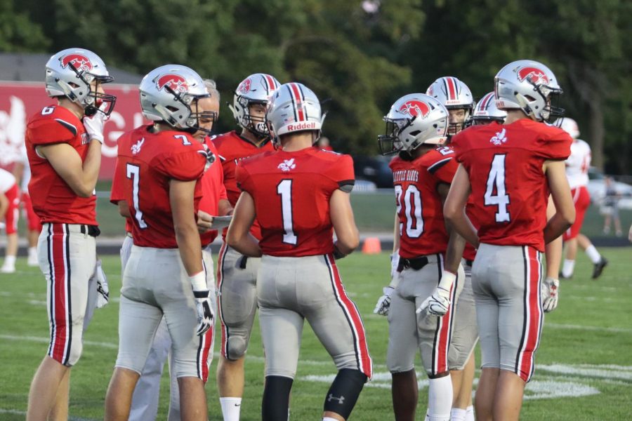 City High football players gather around one of their coaches to hear about plays.