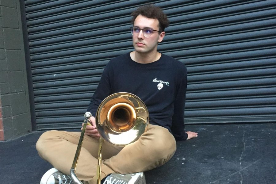 Ryan Carter poses with his trombone in front of a garage.