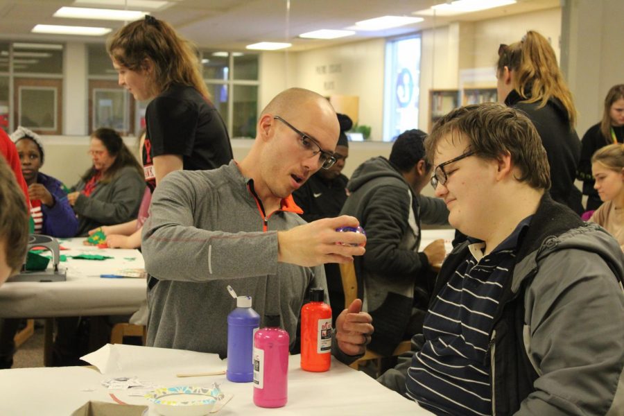 Michael Sabers City High paraprofessional showing buddy how to paint christmas ornaments.