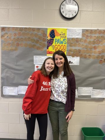 Mrs. Fettweis and Frances Bottorff 22 pose in front of a Get your paws on a good book! poster. 