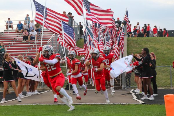 Varsity football team runs out holding flags to commemorate Heroes Night