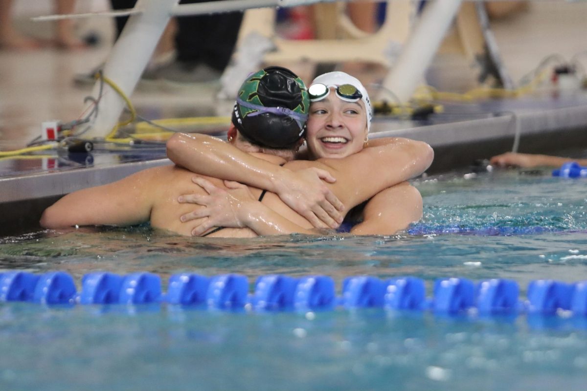 Grace Hoeper 25 reaches over across lanes to hug a swimmer from Iowa City West-Liberty during senior night