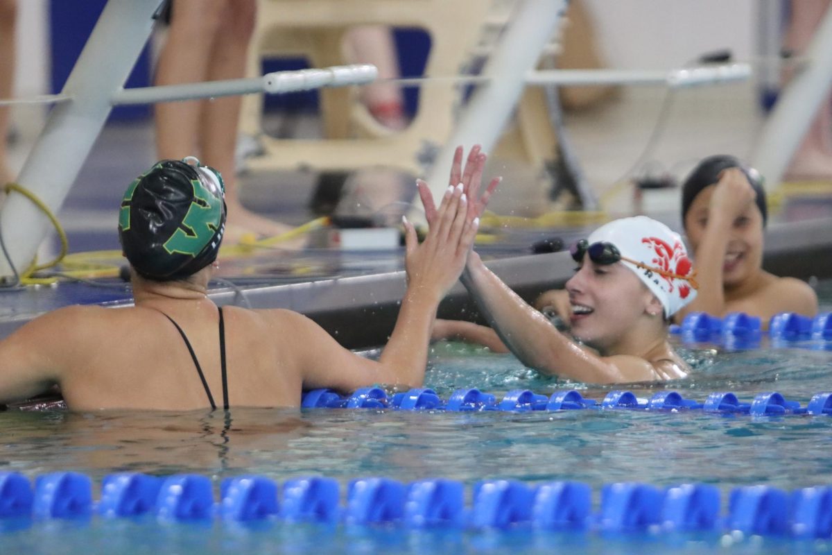 Margalit Frank 24 reaches across the lane to high five a swimmer from West after a race.