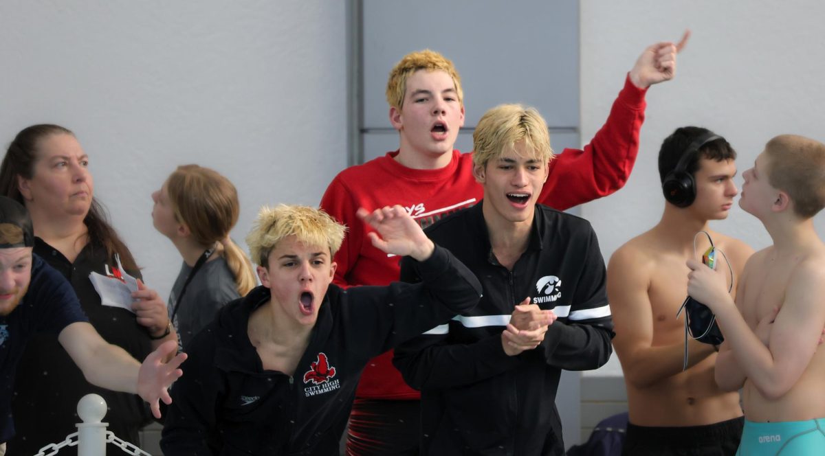 Soren Kenlin, Alex Donovan, and Milo Menzel, varsity swimmers, cheer on their fellow teammates from the side of the pool.